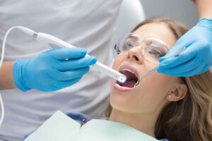 A toddler sits on a caregiver’s lap while a dentist gently checks the child’s small teeth in a bright dental clinic.