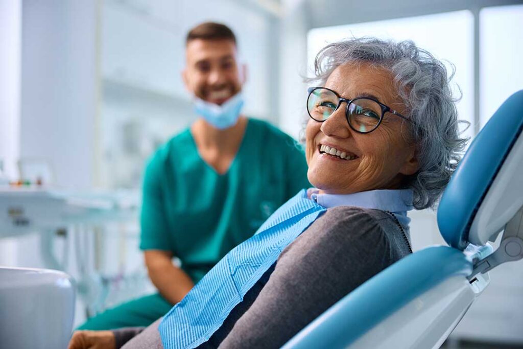 Adult examining stained teeth in a bathroom mirror while holding a cigarette pack nearby.